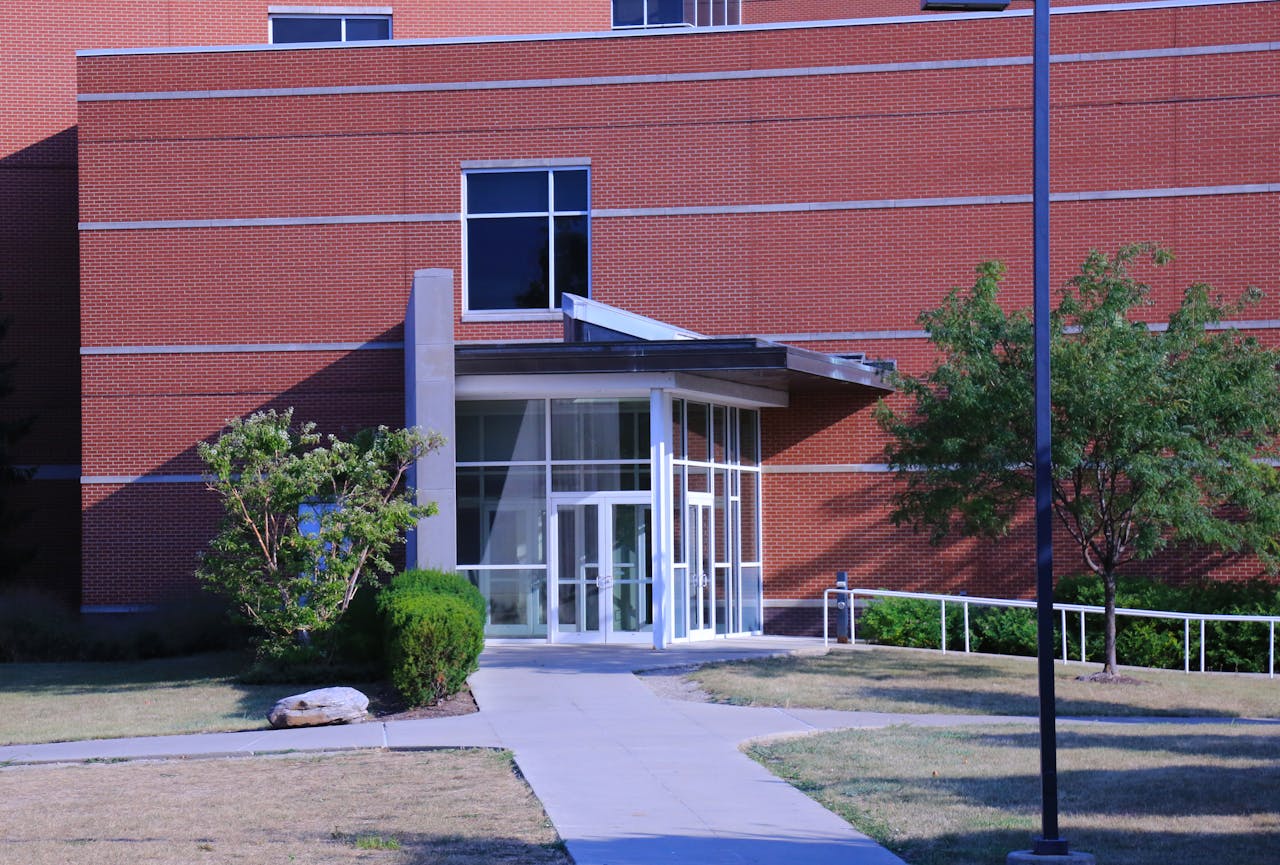 A contemporary brick building exterior with a glass door, garden, and pathway in daylight.